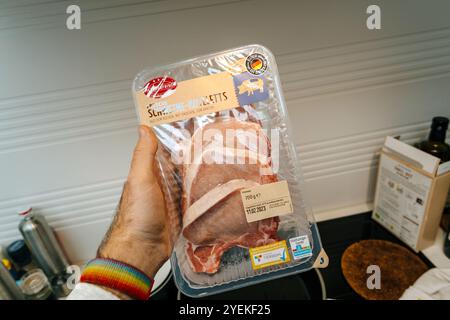 Frankfurt, Deutschland - 3. Februar 2023: Nahaufnahme einer Hand, die ein verpacktes Tablett mit frischem Schweinekotelett in deutscher Sprache hält, mit sichtbarem Verfallsdatum und Tierschutzzertifikat in einer Kücheneinrichtung Stockfoto