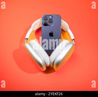 Frankfurt, Deutschland - 29. September 2022: Rückansicht des iPhone 15 Pro Max in Kombination mit Apple AirPods Max, die auf einem leuchtenden orangefarbenen Hintergrund angeordnet sind, unterstreicht das schlanke, moderne Design von Apple Stockfoto