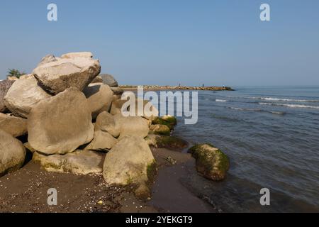 Große Felsen am Ufer des Kaspischen Meeres. Im Hintergrund stehen Fischer am Ufer und fischen mit einer Rute. Stockfoto