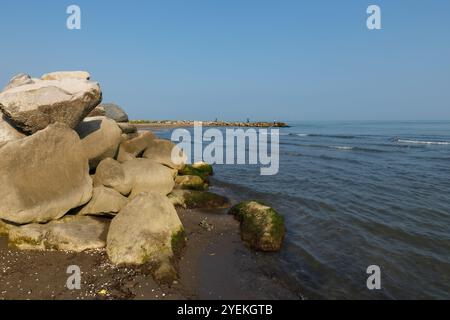 Große Felsen am Ufer des Kaspischen Meeres. Im Hintergrund stehen Fischer am Ufer und fischen mit einer Rute. Stockfoto