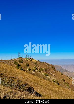 Eine Bergstation auf dem Kamm unter einem klaren blauen Himmel in Kirgisistan, mit verschneiten Hängen und Hügeln im Hintergrund Stockfoto