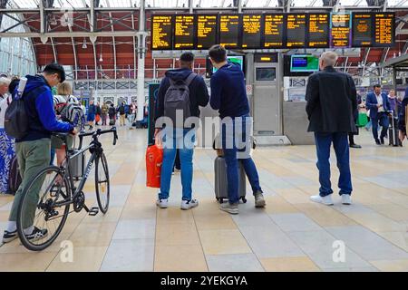 Paddington Bahnhof Rückansicht von männlichen Reisenden, die die Abfahrtszeiten auf großen Zieltafeln mit Radfahrer in der Hand haben London England UK Stockfoto