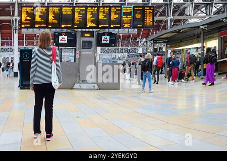 Rückansicht einsame Frauen, die an den Bahnabfahrtstafeln im Paddington Station Terminal in London, England, Großbritannien, vorbeischauen Stockfoto