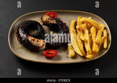 Gegrillte Kraken-Tentakel mit Kartoffeln und Kräutern auf einem Teller. Auf schwarzem Hintergrund. Stockfoto