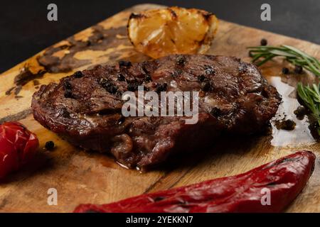 Leckerer gegrillter Rib Eye Black Angus serviert mit Pfeffer und Kräutern auf Holzbrett. Stockfoto