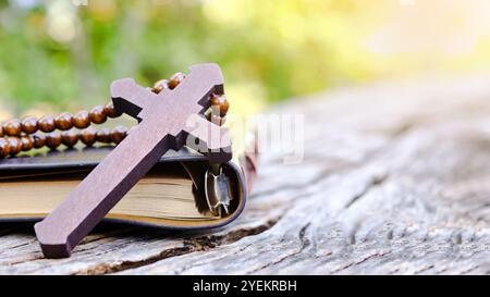 Dunkelrotes Holzkreuz, das sich an ein altes offenes Buch lehnt, das die Verbreitung der Liebe Jesu Christi unter Christen symbolisiert, die den Glauben und die Hingabe widerspiegelt Stockfoto