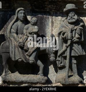 Flug nach Ägypten, geformt in den 1580er Jahren Szene auf dem Kalvarium in der Pfarrei in der Nähe der Kirche Saint Miliau im Dorf Guimiliau, Finistère, Bretagne, Frankreich. Maria, die auf einem Esel auf einem Seitensattel sitzt, streichelt den kleinen Fuß des Jesuskindes. Joseph, gekleidet als Herr aus dem 16. Jahrhundert, führt den Esel an; er hält eine Tasche in der einen Hand und einen Pilgerstab in der anderen. Stockfoto