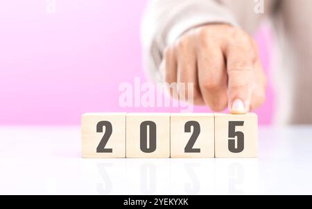 Hand ersetzt „2024“ durch „2025“ mithilfe von Zahlenblöcken, die den Übergang ins neue Jahr symbolisieren und Veränderungen, Fortschritte und den laufenden Pas darstellen Stockfoto