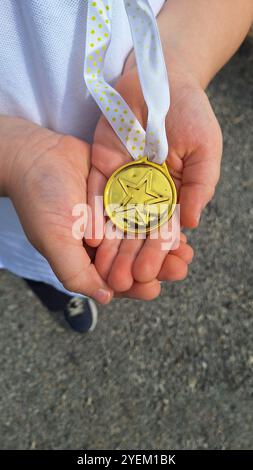 Ein Kind, das stolz eine Goldmedaille mit einem Stern auf dem ersten Platz hält. Stockfoto