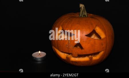 Geschnitzter Kürbis und Teelicht auf schwarzem Hintergrund, Jack-o-Laterne halloween-Tapete mit Kopierraum Stockfoto