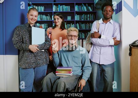 Eine Gruppe verschiedener Studenten, die zusammen stehen und Bücher und Rucksäcke in einer Bibliothek halten. Sie lächeln und blicken in die Kamera, strahlen Positivität und Selbstvertrauen aus Stockfoto