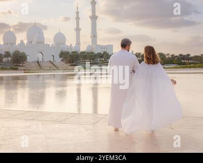 Reisen Sie in die Vereinigten Arabischen Emirate, Abu Dhabi. Arabisches Paar besucht den Park in der Nähe der Großen Moschee in Abu Dhabi in traditioneller Kleidung. Stockfoto