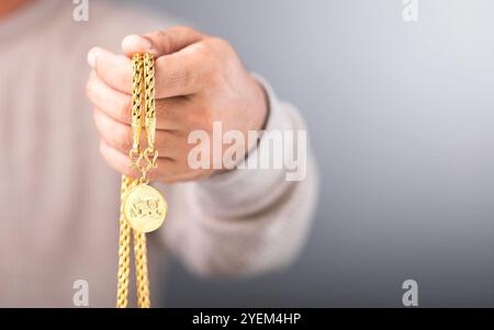 Nahaufnahme eines Mannes, der eine goldene Halskette in der Hand hält, die das Konzept des Goldmarktwerts symbolisiert. Spiegelt die Überprüfung der Echtheit des Goldes wider, e Stockfoto