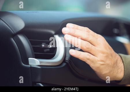 Der Autobesitzer überprüft die Klimaanlage, indem er die kühle Luft aus der Entlüftung spürt, nachdem das Fahrzeug überflutet wurde. Konzept der Fahrzeugwartung, Stockfoto