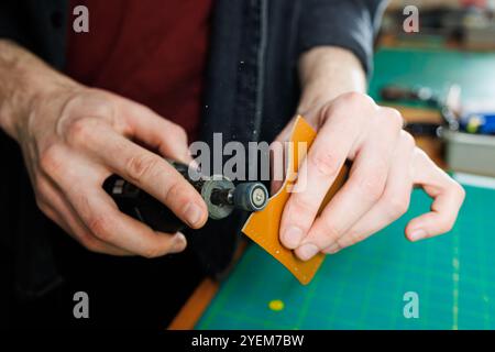 Die Hand eines Mannes hält Lederstücke für eine Ledertasche in seiner Werkstatt. Der Prozess der Arbeit mit naturbraunem Leder. Der Handwerker hält den Stockfoto