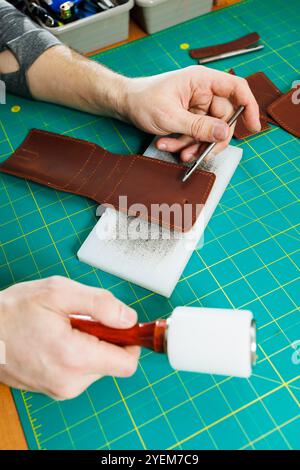 Die Hand eines Mannes hält Lederstücke für eine Ledertasche in seiner Werkstatt. Der Prozess der Arbeit mit naturbraunem Leder. Der Handwerker hält den Stockfoto