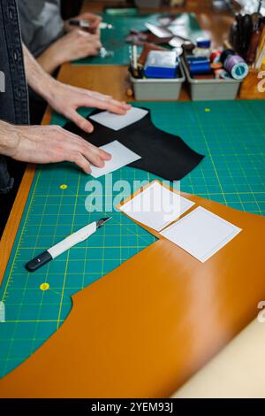 Die Hand eines Mannes hält Lederstücke für eine Ledertasche in seiner Werkstatt. Der Prozess der Arbeit mit naturbraunem Leder. Der Handwerker hält den Stockfoto