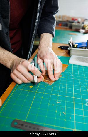 Die Hand eines Mannes hält Lederstücke für eine Ledertasche in seiner Werkstatt. Der Prozess der Arbeit mit naturbraunem Leder. Der Handwerker hält den Stockfoto