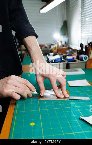 Die Hand eines Mannes hält Lederstücke für eine Ledertasche in seiner Werkstatt. Der Prozess der Arbeit mit naturbraunem Leder. Der Handwerker hält den Stockfoto