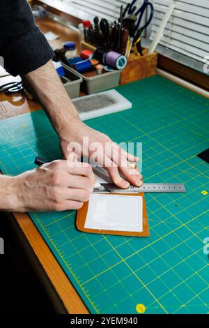 Die Hand eines Mannes hält Lederstücke für eine Ledertasche in seiner Werkstatt. Der Prozess der Arbeit mit naturbraunem Leder. Der Handwerker hält den Stockfoto