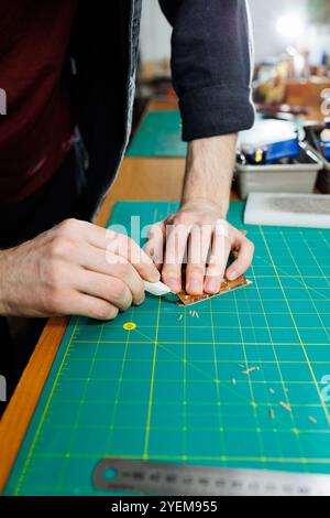 Die Hand eines Mannes hält Lederstücke für eine Ledertasche in seiner Werkstatt. Der Prozess der Arbeit mit naturbraunem Leder. Der Handwerker hält den Stockfoto