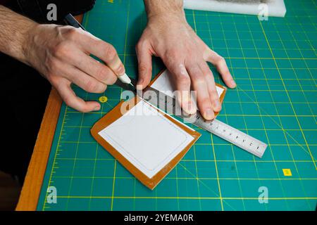 Die Hand eines Mannes hält Lederstücke für eine Ledertasche in seiner Werkstatt. Der Prozess der Arbeit mit naturbraunem Leder. Der Handwerker hält den Stockfoto