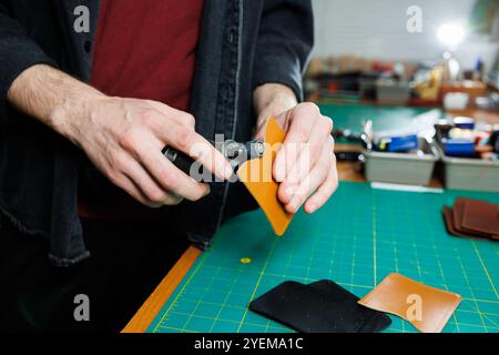Die Hand eines Mannes hält Lederstücke für eine Ledertasche in seiner Werkstatt. Der Prozess der Arbeit mit naturbraunem Leder. Der Handwerker hält den Stockfoto
