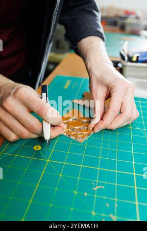 Die Hand eines Mannes hält Lederstücke für eine Ledertasche in seiner Werkstatt. Der Prozess der Arbeit mit naturbraunem Leder. Der Handwerker hält den Stockfoto