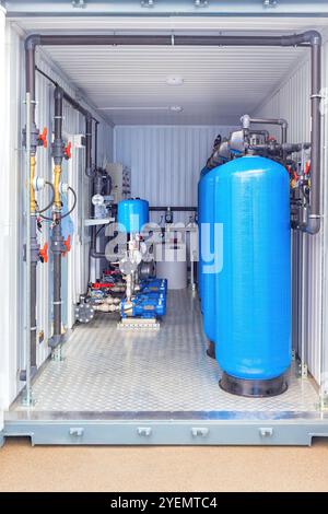 Wasserfiltrationssystem im Industriecontainer mit blauen Tanks, Rohren, Maschinen, Ventilen und Reinwasserlösung. Stockfoto