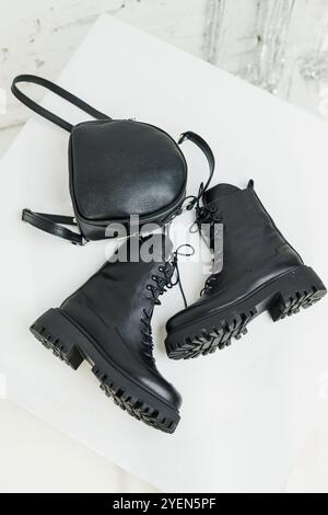 Schwarze Lederstiefel für Damen und ein schwarzer Lederrucksack stehen auf weißem Hintergrund. Damenmode Stockfoto