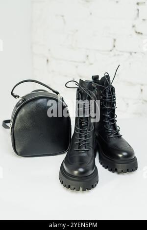 Schwarze Lederstiefel für Damen und ein schwarzer Lederrucksack stehen auf weißem Hintergrund. Damenmode Stockfoto