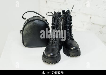 Schwarze Lederstiefel für Damen und ein schwarzer Lederrucksack stehen auf weißem Hintergrund. Damenmode Stockfoto