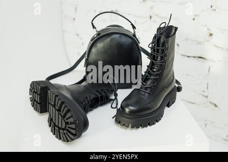 Schwarze Lederstiefel für Damen und ein schwarzer Lederrucksack stehen auf weißem Hintergrund. Damenmode Stockfoto