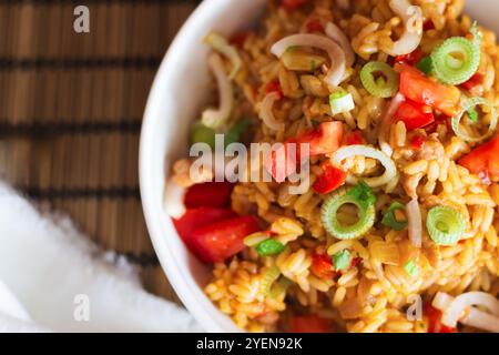 Nahaufnahme einer Schüssel mit herzhaftem Reis und zartem Fleisch, belegt mit frischen Tomatenstücken und geschnittenen Schalotten, die ihr einen Hauch von Farbe und fla verleihen Stockfoto