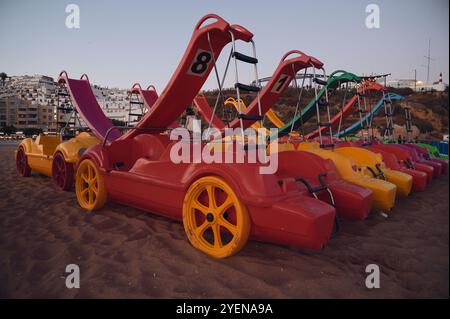 Bunte Tretboote stehen am Sandstrand von Albufeira an, bereit für Abenteuer am Meer, wenn der Tag nachlässt Stockfoto