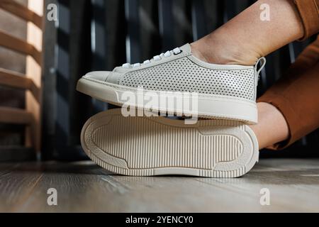 Schlanke weibliche Beine in Hose in Nahaufnahme in beigefarbenen, legeren Sneakers. Lederschuhe für Damen. Stockfoto