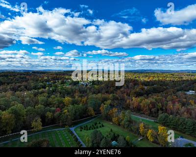 Weite Felder und farbenfrohe Bäume erstrecken sich über die Landschaft und zeigen die Schönheit des Herbstes mit einem dramatischen Himmel. Die Szene fängt eine friedliche ländliche Landschaft mit natürlichem Charme ein. Stockfoto