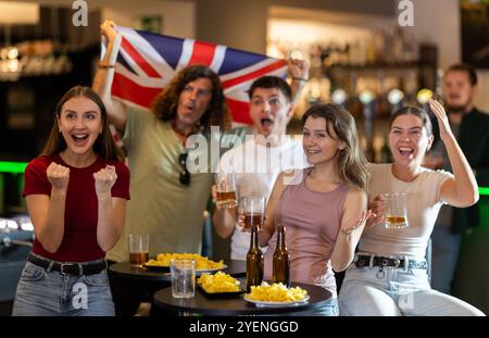 Emotionale britische Fans mit Nationalflagge sehen das Spiel im Fernsehen mit Interesse und kommentieren aktiv Stockfoto