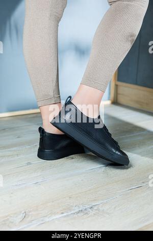 Kollektion von Damenschuhen. Schwarze Lederschuhe an den Füßen von Frauen. Weibliche Füße in bequemen, legeren Sandalen Stockfoto