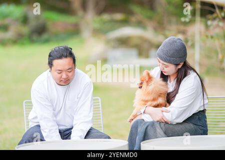 Ein koreanischer Mann und eine Japanerin, beide im Alter von 30 Jahren und ein verheiratetes Paar, genießen in einem stilvollen Café im Herbst einen Brunch mit drei Hunden Stockfoto