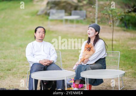 Ein koreanischer Mann und eine Japanerin, beide im Alter von 30 Jahren und ein verheiratetes Paar, genießen in einem stilvollen Café im Herbst einen Brunch mit drei Hunden Stockfoto