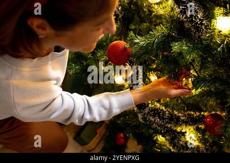 Weihnachtsbaumschmuck, Seniorin, die mit Sorgfalt und Freude Ornamente setzt, zu Hause. Feiertage, Festtage, Dekoration, Feier, Tradition, Familie Stockfoto