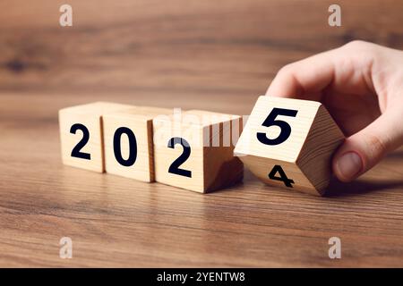 Neujahr 2025. Frau, die Holzwürfel auf dem Tisch dreht, Nahaufnahme Stockfoto