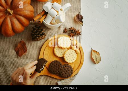 Schaffen Sie eine warme Herbstatmosphäre, indem Sie Kekse und Marshmallows auf einem rustikalen Holzbrett arrangieren Stockfoto