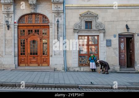 Lemberg, Ukraine, 14. Januar 2015: Eine Frau in traditioneller Kleidung steht in der Nähe eines historischen Gebäudes und spielt Flöte. Fahnen hängen über ihnen und fügen einen Sen hinzu Stockfoto