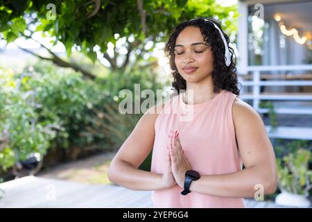 Junge Frau, die draußen meditiert, Kopfhörer und Smartwatch trägt, sich friedlich fühlt. Meditation, Achtsamkeit, Entspannung, Ruhe, Wellness, sere Stockfoto