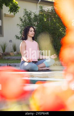 Frau meditiert draußen auf Yogamatte, genießt friedliche Gartenumgebung. Meditation, Entspannung, Wellness, Ruhe, Achtsamkeit, Natur Stockfoto