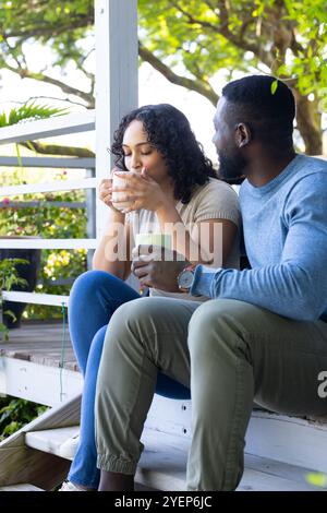 Entspannen Sie auf der Veranda, multirassische Paare genießen Kaffee zusammen am friedlichen Morgen. Lifestyle, Entspannung, Zweisamkeit, draußen, Ruhe Stockfoto
