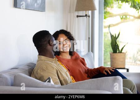 Lächelndes multirassisches Paar, das sich auf dem Sofa zu Hause entspannt und einen gemütlichen Nachmittag zusammen genießt. Entspannung, Lebensstil, Zweisamkeit, Beziehung, Bindung Stockfoto