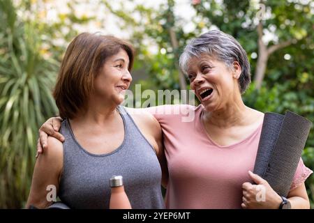 Ältere Freundinnen lachen zusammen im Freien, halten Yogamatten und Trinkflasche. Fitness, Bewegung, Wellness, Freundschaft, Lifestyle, Genuss Stockfoto